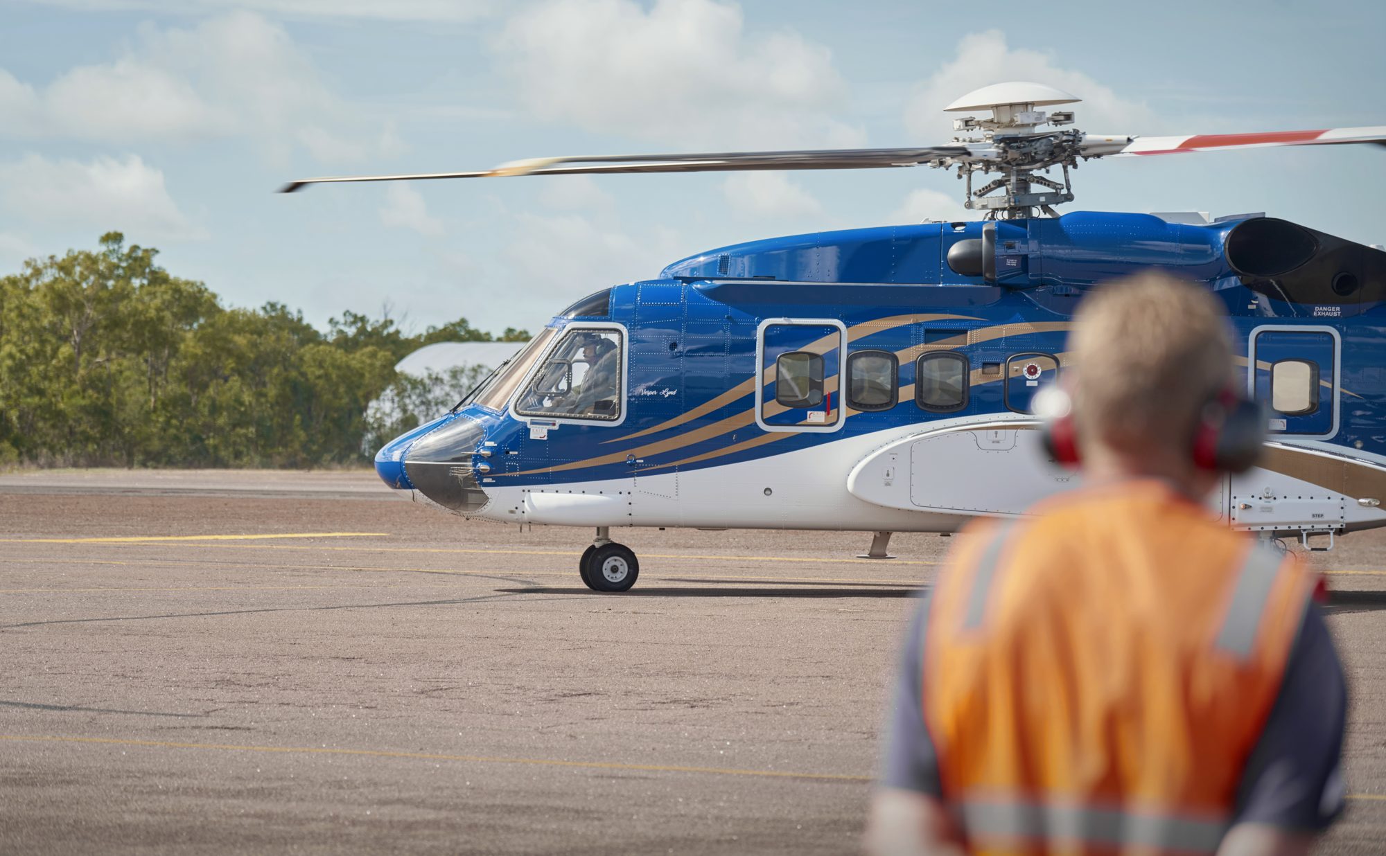 A marshaller in orange hi-vis guiding a helicopter on the apron